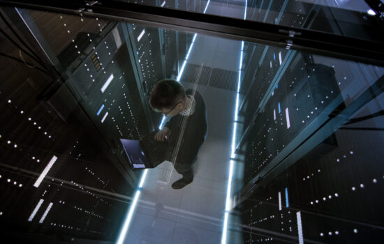 Top View Through the Glass of IT Engineer Working with Laptop in Data Center Full of  Active Rack Servers.